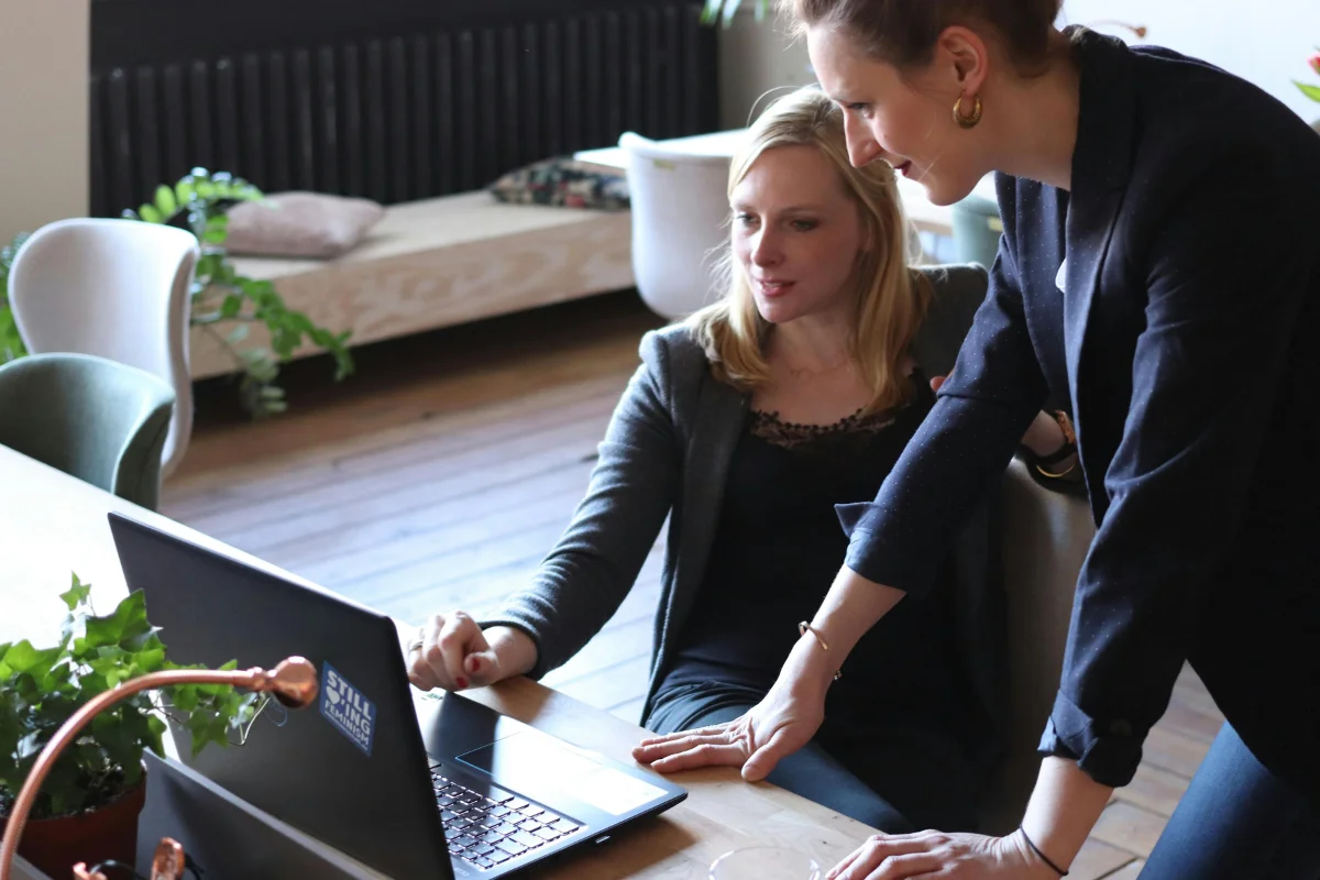 Two Women Looking At a Laptop Screen As They Discuss Something. Side Hustles.