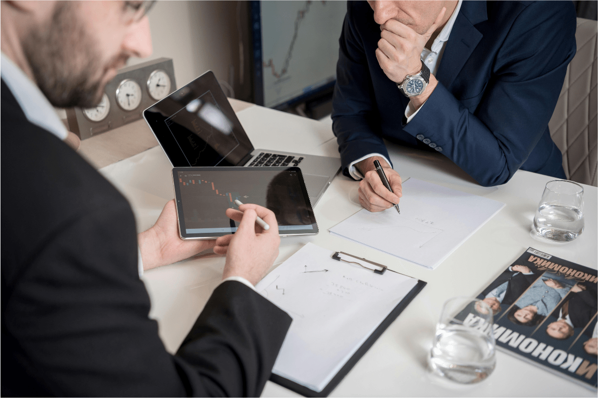 Two individuals discussing a business plan with a laptop and tablet, illustrating key steps on how to start a catering business