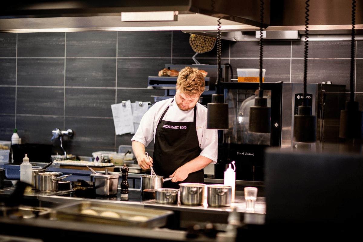 A person whisking ingredients in a pot in a commercial kitchen, completing food preparation for a catering business, highlighting steps on how to start a catering business.