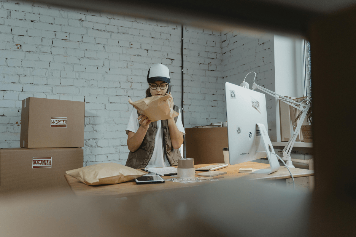 Promote Your Business - How to Start a Box Truck Business A Woman is Checking a Parcel While Standing in a Warehouse Where Boxes Can be Seen in the back Illustrating How to Start a Box Truck Business