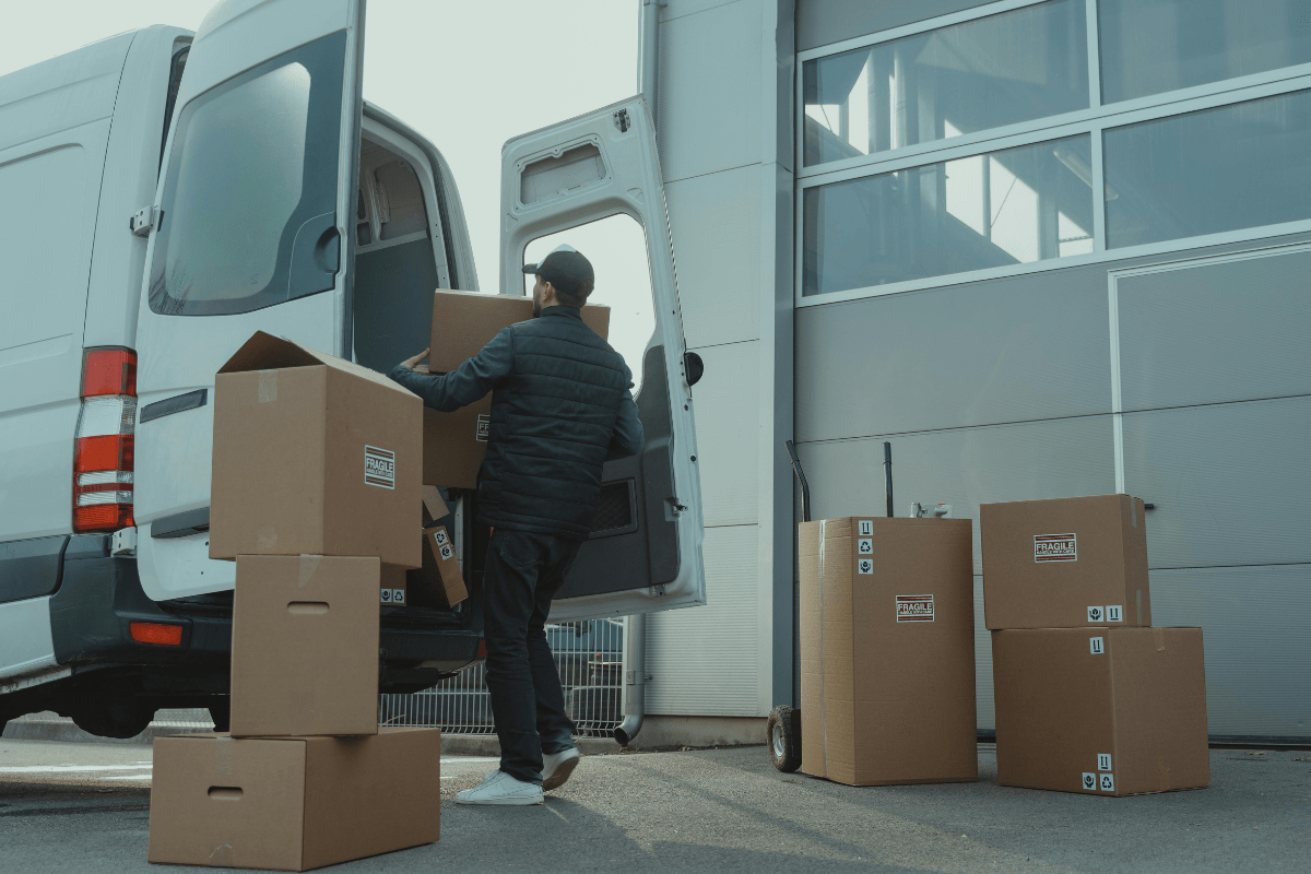 Man unloading cardboard boxes from the back of an open box truck, displaying the logistics involved in how to start a box truck business.