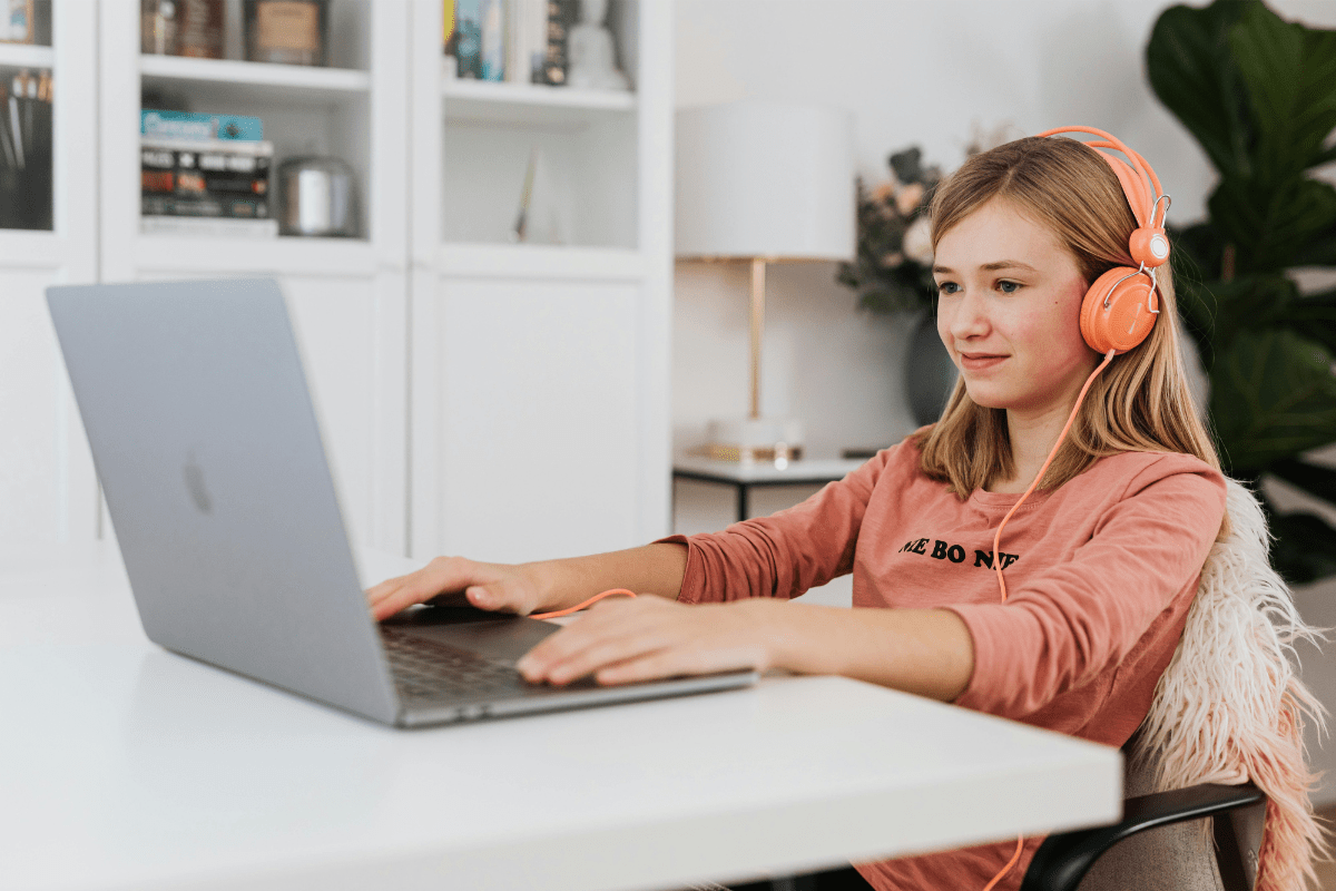 Working on YouTube Channel - How to Make Money As a Kid A Teenage Girl Sitting on a Chair With her Headphone Connected to a Laptop Placed In Front of her on the Table Illustrating How to Make Money As a Kid.