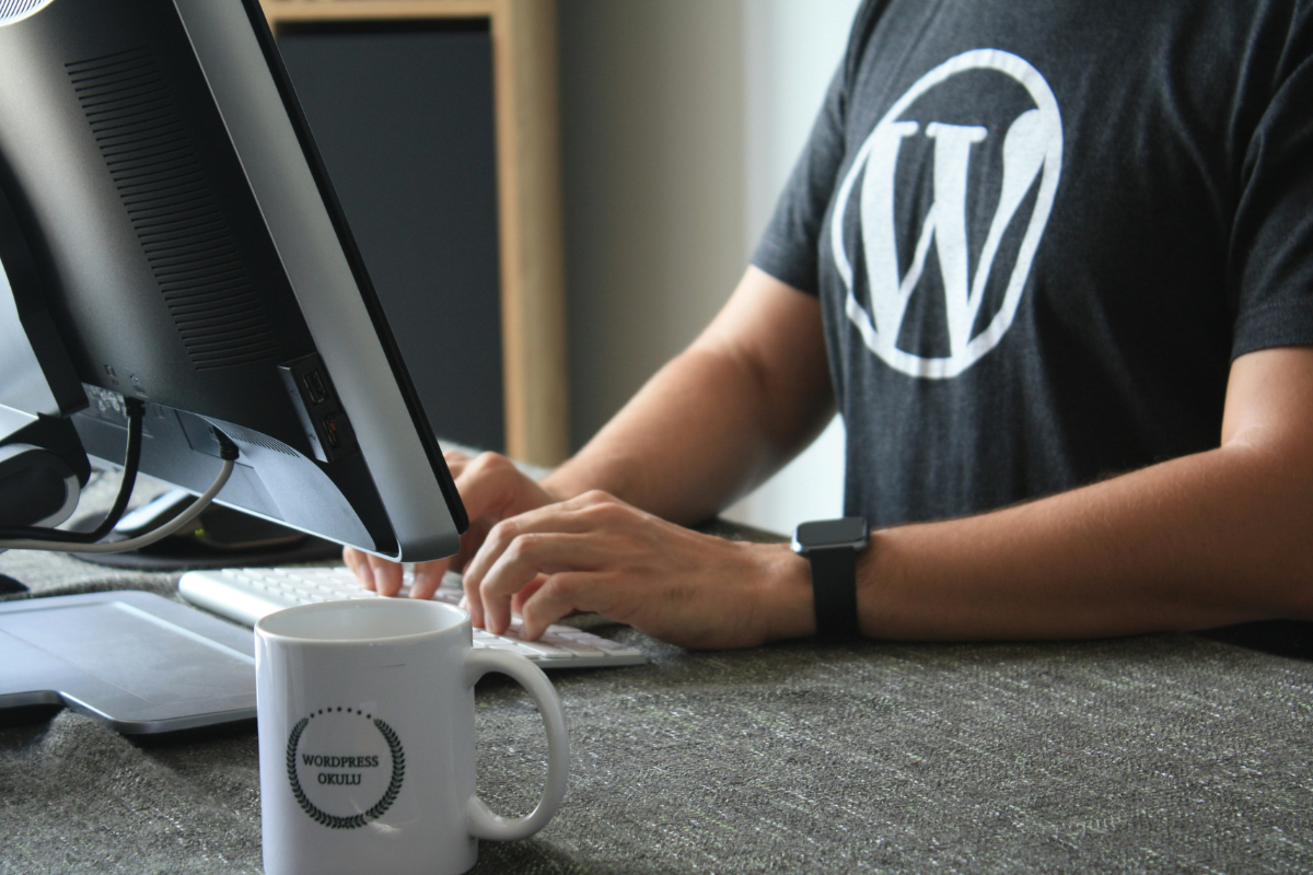 A Person's Wearing a Shirt With WordPress Logo Working On a Laptop Illustrating Best Place to Sell Digital Products Online 