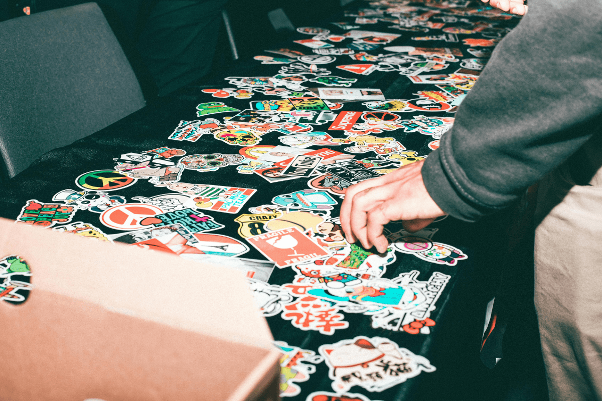 Sell Custom Stickers - Side Hustles for Teens The Hands of Person Can Be Seen Picking Some Stickers Scattered on a Table Illustrating Side Hustles for Teens