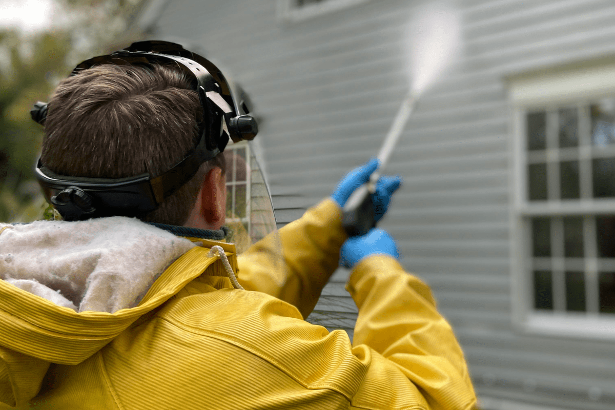 A Man Can Be Seen Power Washing the Exterior of a House Illustrating Handyman Side Hustle