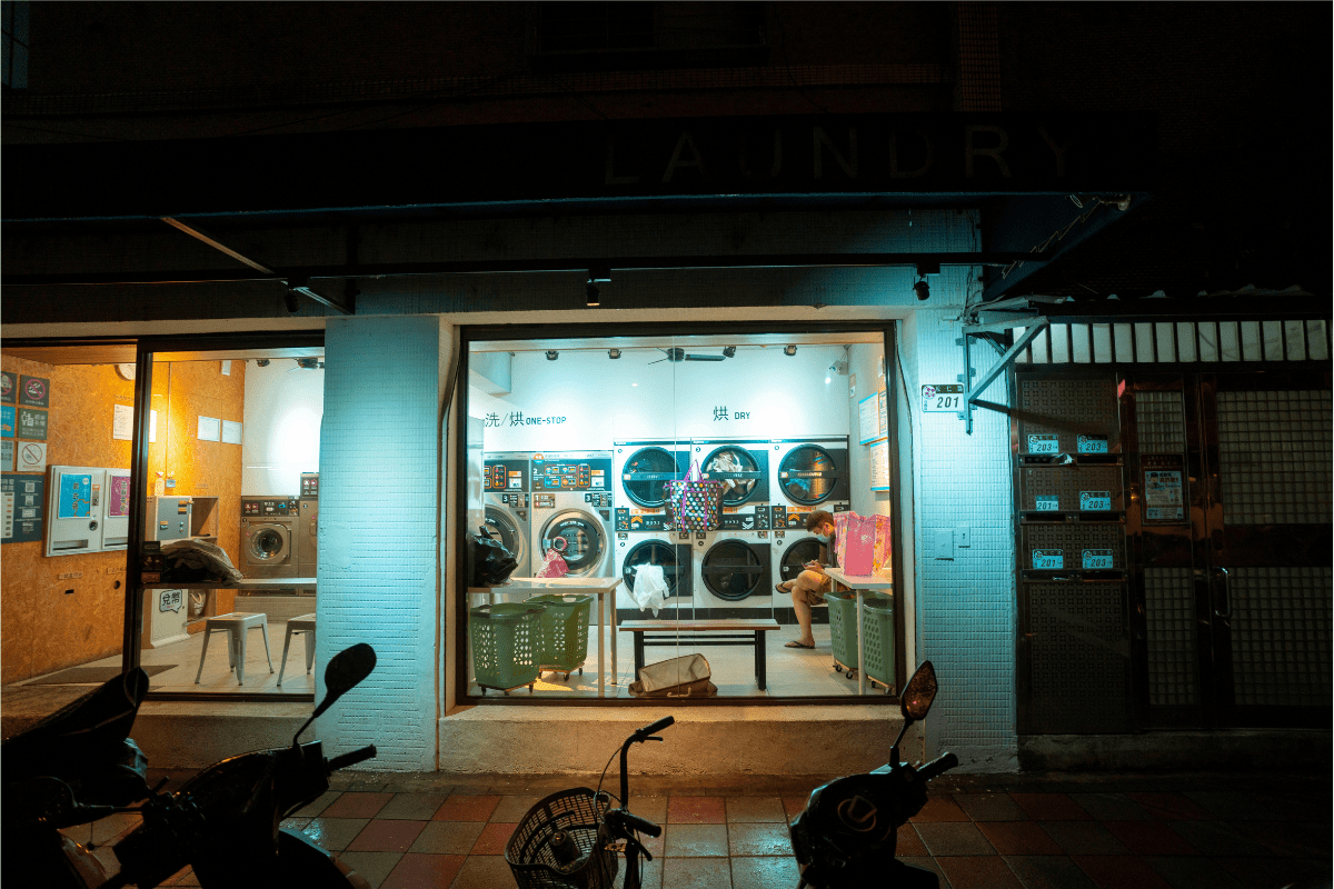 A Laundromat Can Be Seen From a Glass Window Standing on a Side Walk Illustrating How to Start a Coin Laundromat Business.