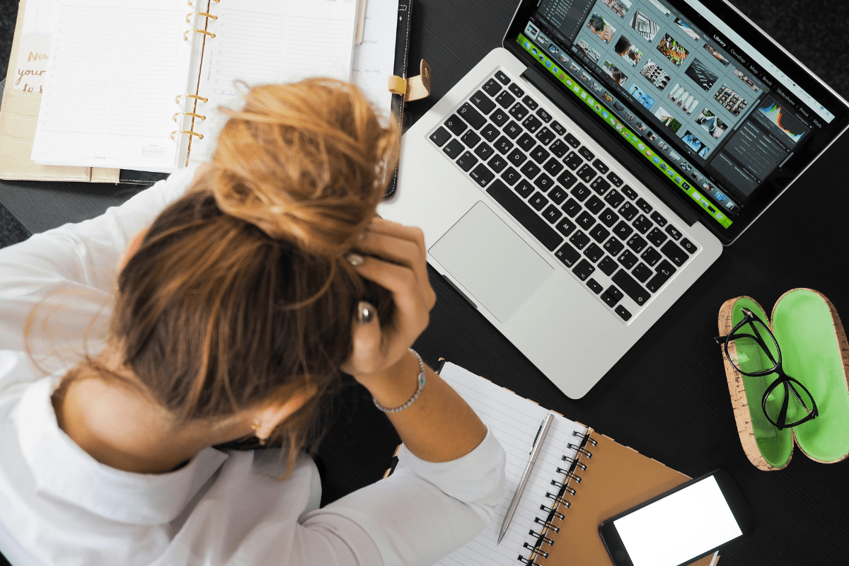 A Woman Can be Seen from a Top Angle Holding her Head While Working on Her Laptop Illustrating Side Hustles for single Moms