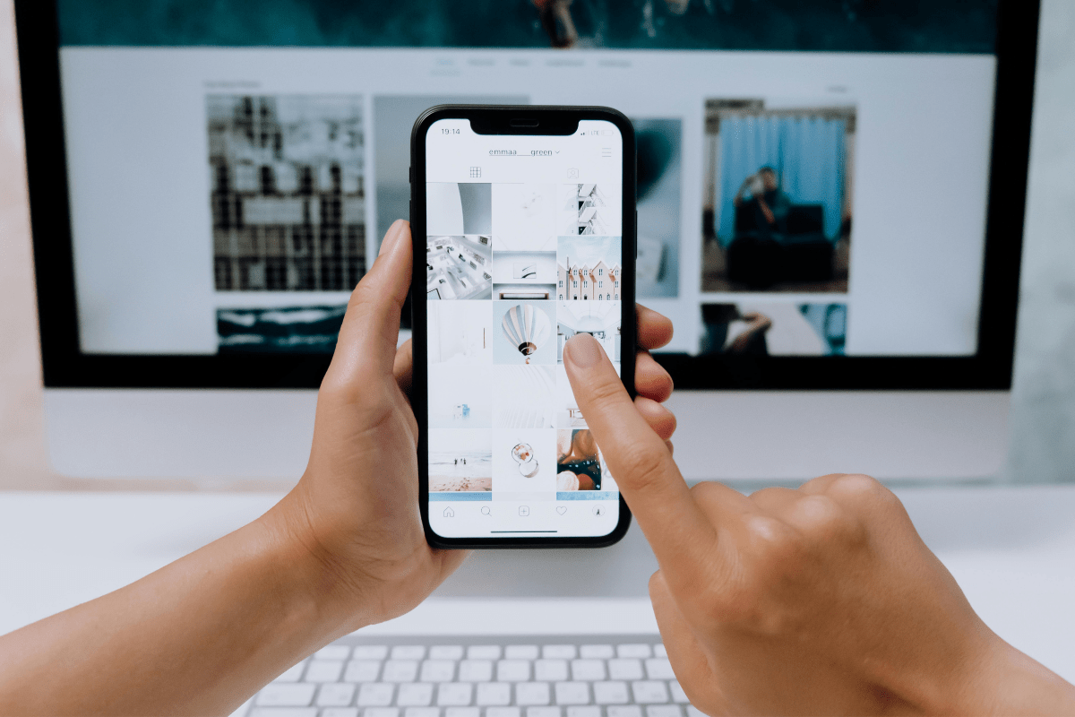 Promotion - How to Start a Photography Business A Person Holding Phone Against a Computer Screen Scrolling Through Some Photographs Illustrating How to Start a Photography Business