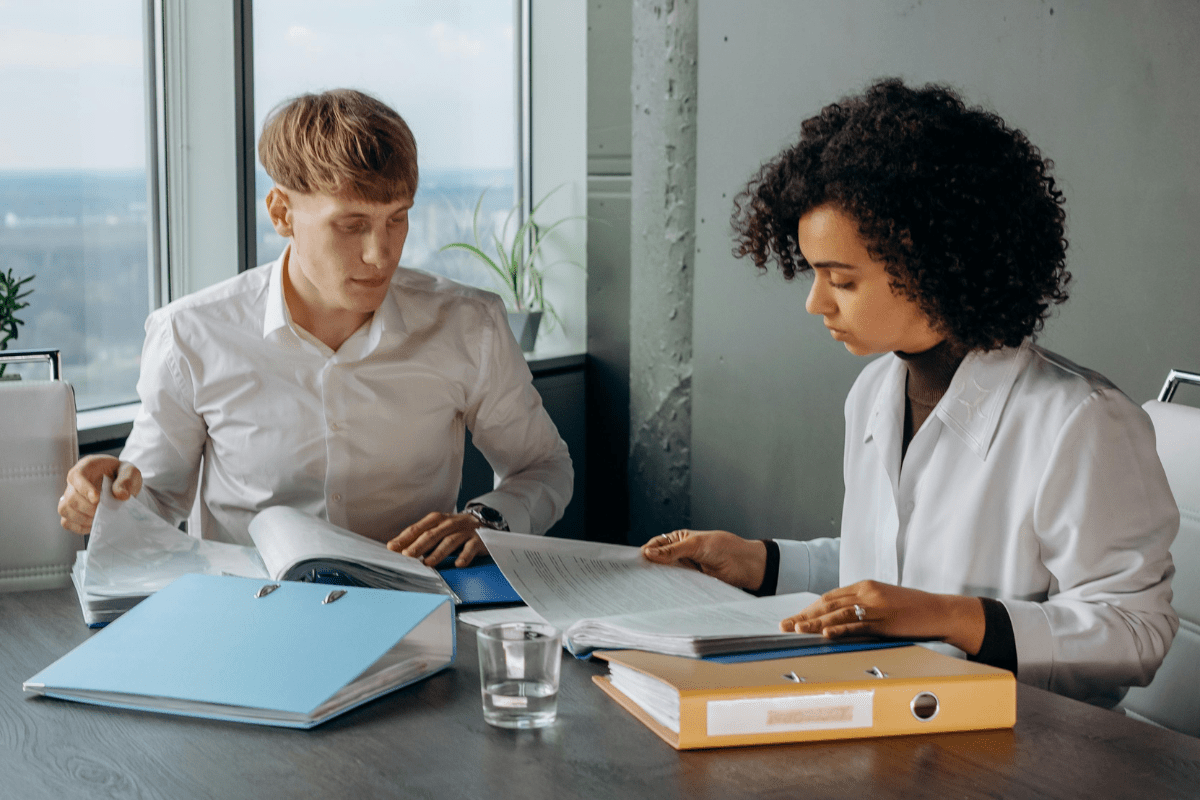 Offer Consulting Services - Best Side Hustles for Accountants Two Individuals Are Sitting in an Office Room Going Through Paper Work Illustrating Best Side Hustles for Accountants