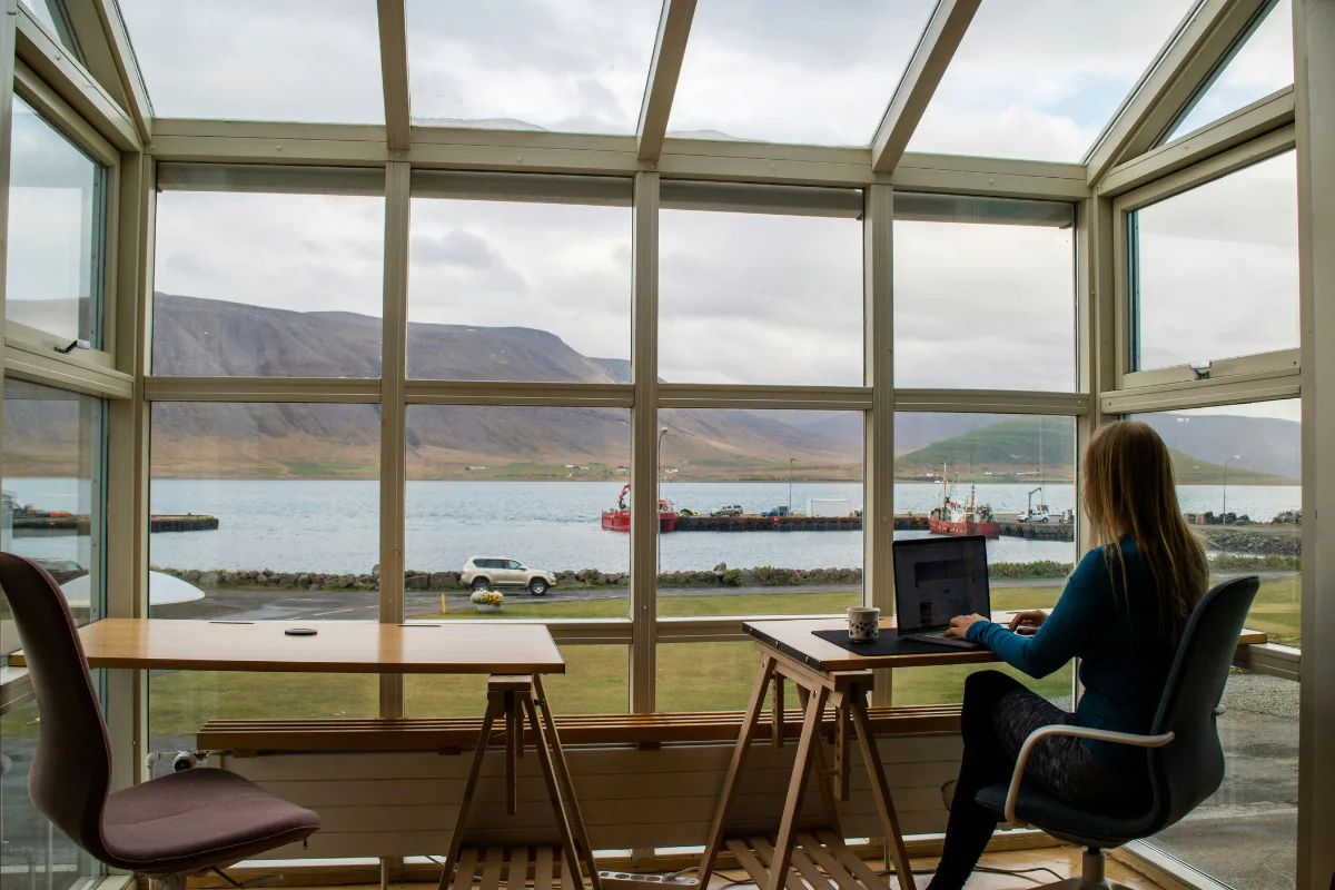 A Woman Working on Her Laptop Sitting By the Window Illustrating Remote Side Hustles