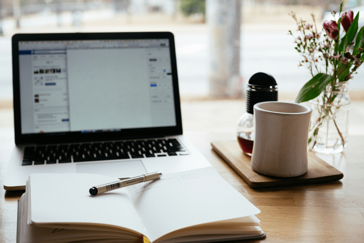 A Laptop is Placed on a Table With An Open Notebook and Pen Illustrating Side Hustle Apps to Make Money