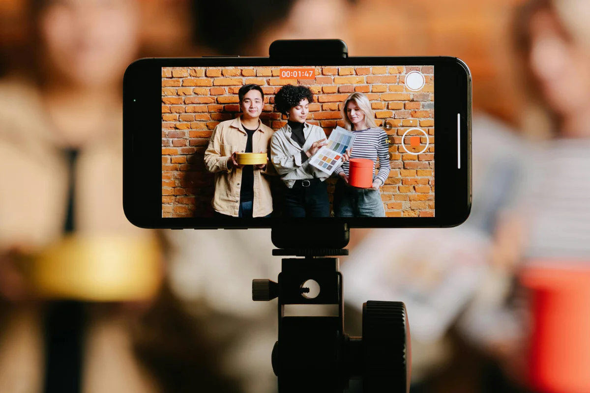 Content Creation - Side Hustle Apps Mobile Phone Screen Can be Seen Set on a Tripod Where Three Person Can be Seen Illustrating Side Hustle Apps