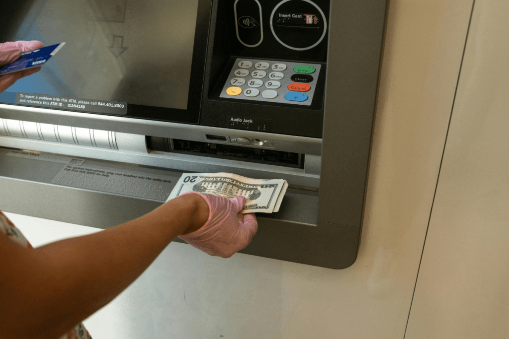 A Person Hands Can Be Seen Standing in Front of an ATM Holding Card in One Hand while Cash in the Other Hand Illustrating ATM Business.