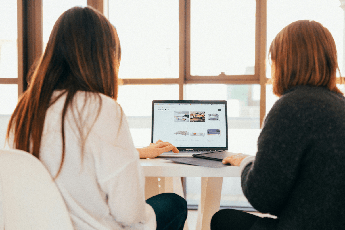 Two Women Can Be Seen From The Back Sitting Facing a Laptop Illustrating Healthcare Agency as One of the Best Business Ideas for Nurses
