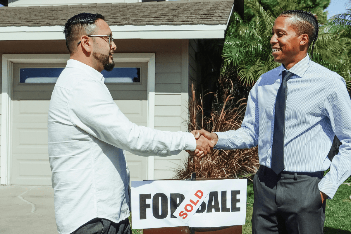 Two Persons Can Be Seen Shaking Hands In Front of a House Illustrating Best Side Hustles for Real Estate Agents